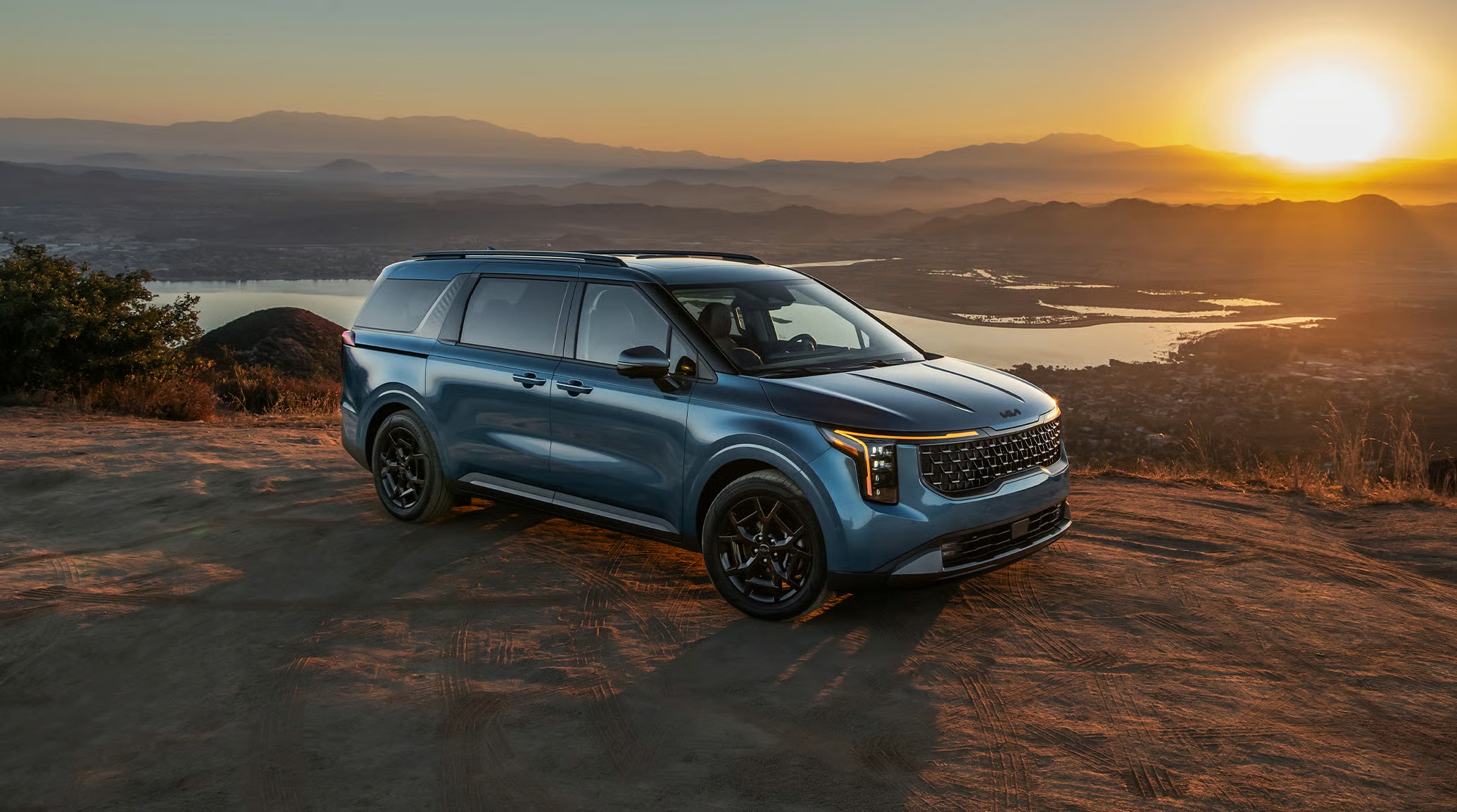 Rear three-quarter view of blue Kia Carnival minivan at sunset