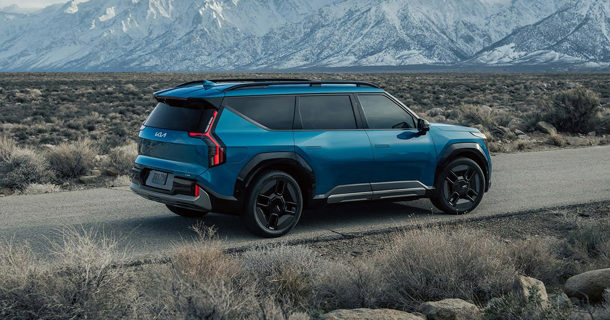 Blue Kia EV9 electric SUV parked in desert landscape with mountains
