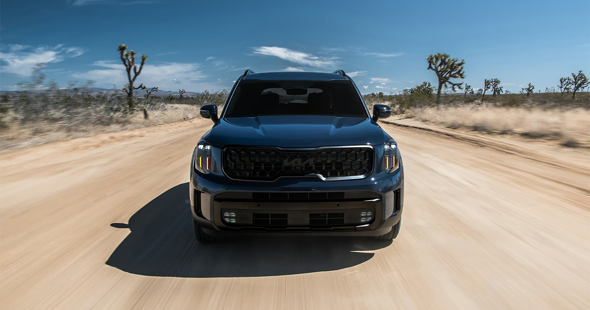 Blue Kia Telluride SUV in desert landscape with Joshua trees and cacti