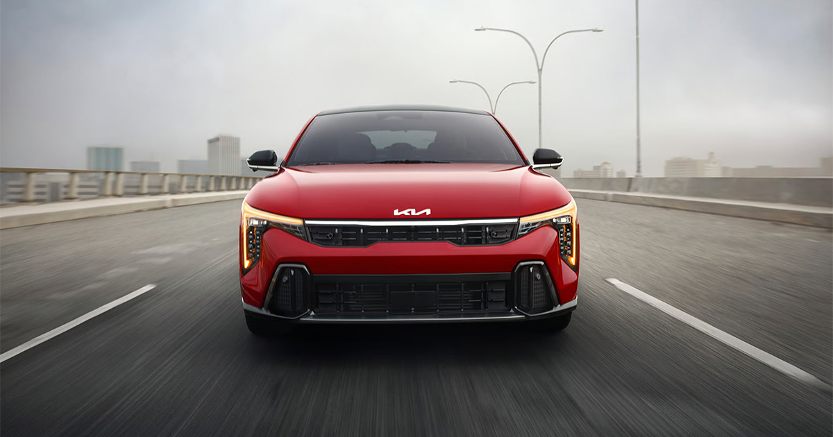Red Kia K4 sedan front view on highway with city skyline