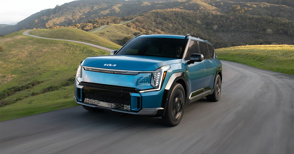 Blue Kia EV9 electric SUV driving on winding country road