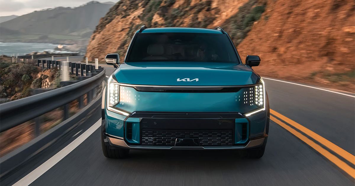 Blue Kia EV9 electric SUV on coastal highway with ocean views