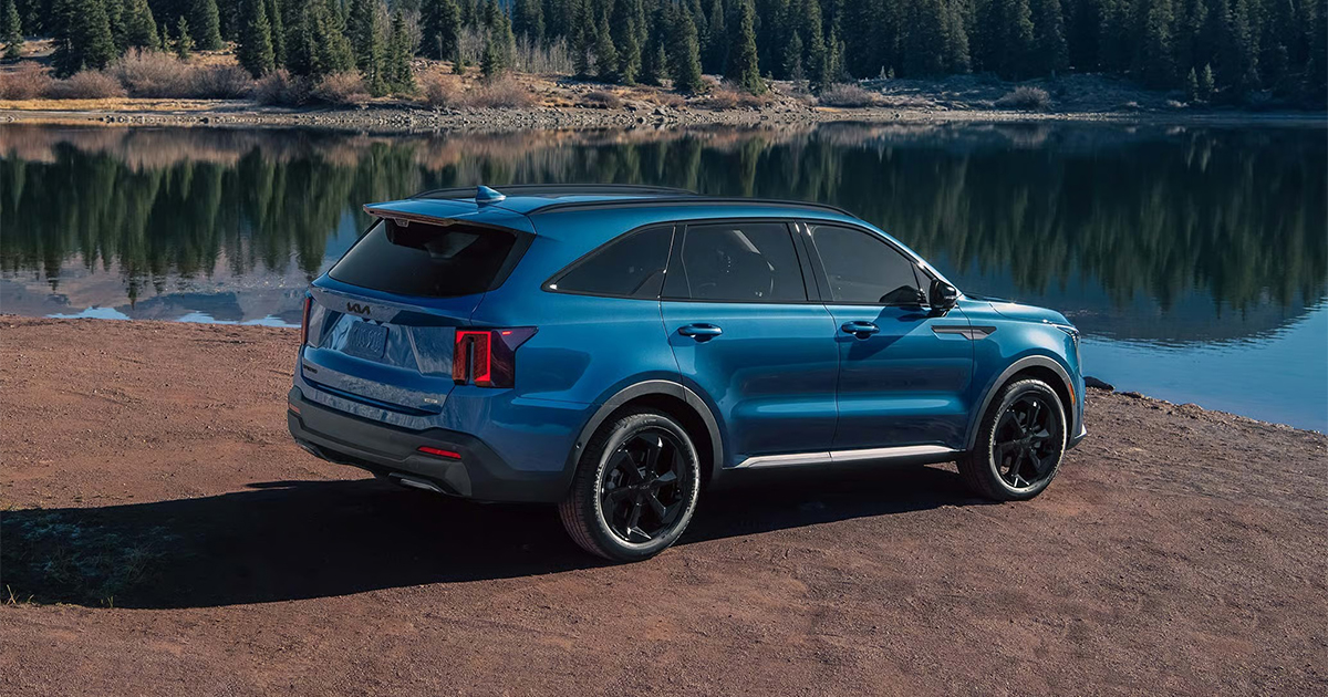 Rear view of blue Kia Sorento Hybrid SUV beside reflective mountain lake