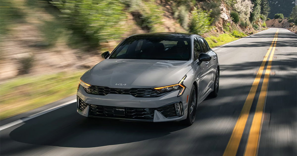 Gray Kia K5 sedan driving on winding mountain highwa