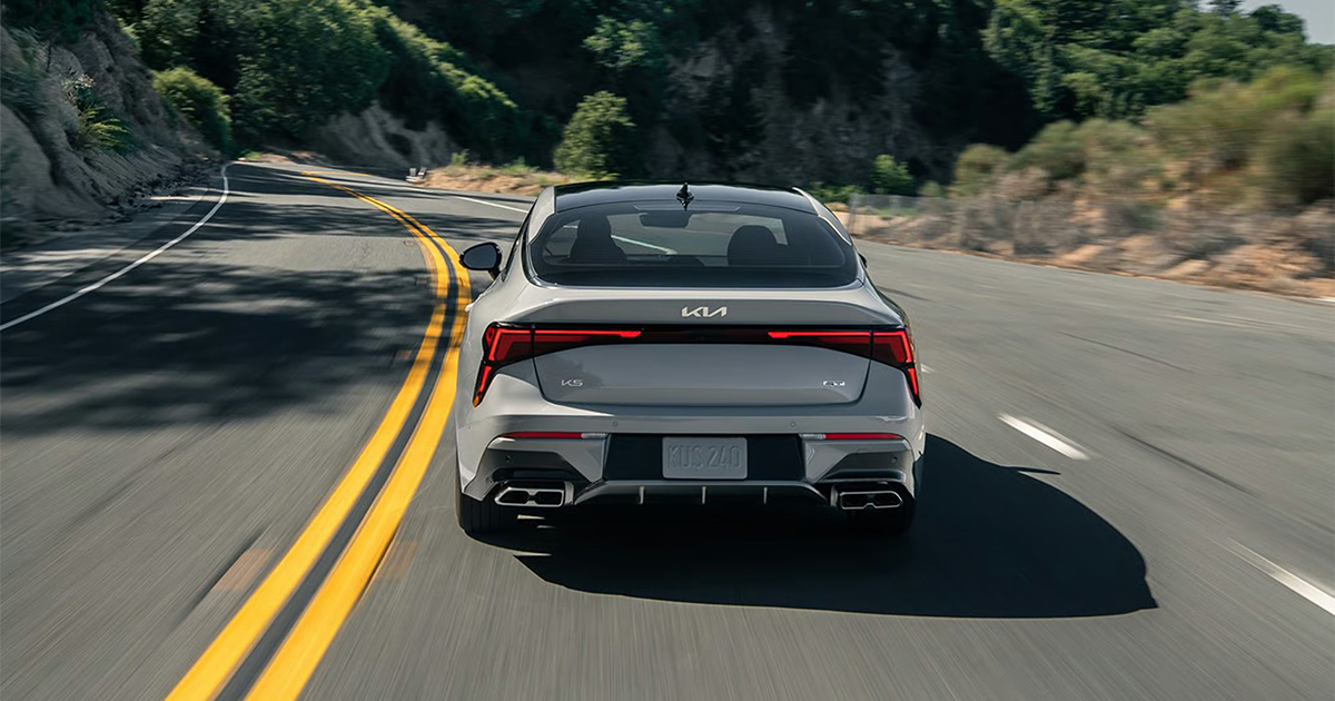 Rear view of white Kia K5 sedan on curved mountain road