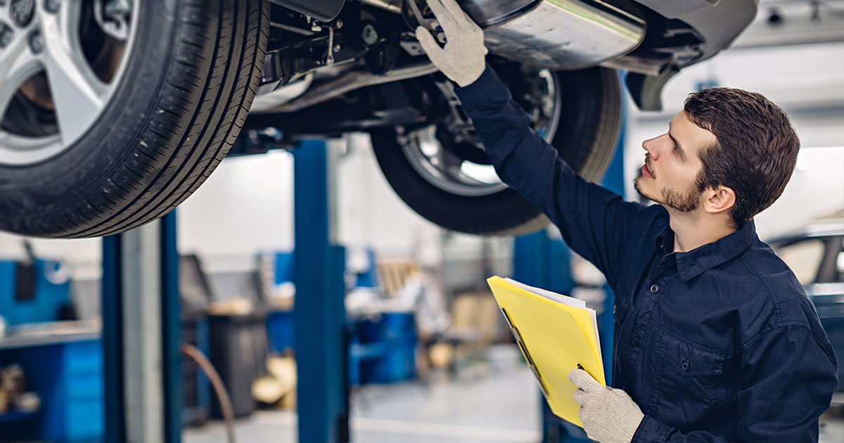 Automotive technician inspecting lifted vehicle with clipboard