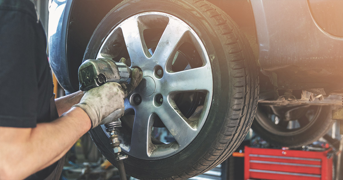 Mechanic using impact wrench to service car tire in auto shop