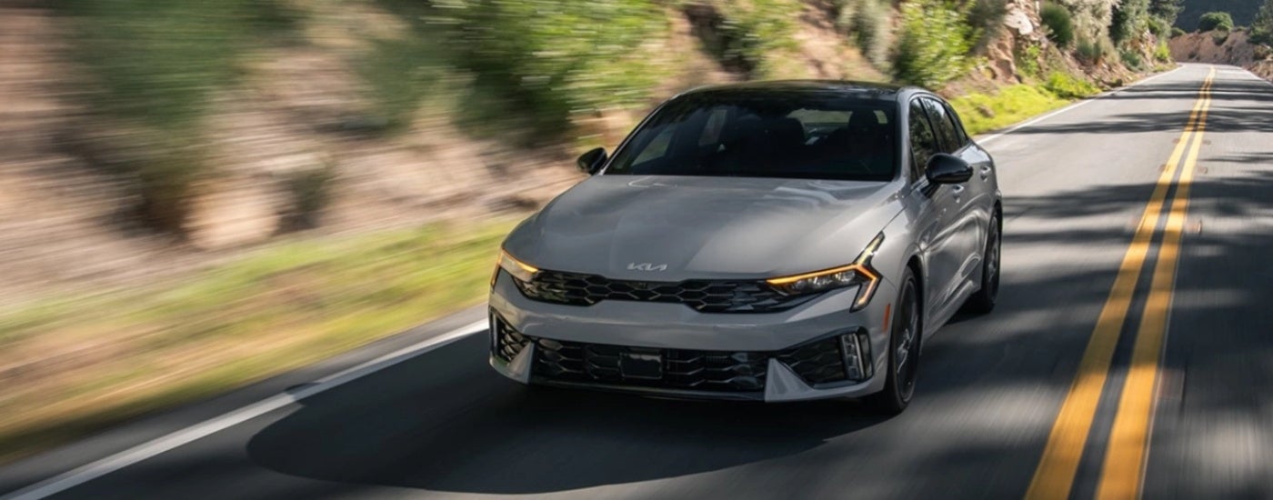 Grey 2025 Kia K5 for sale driving on an open road