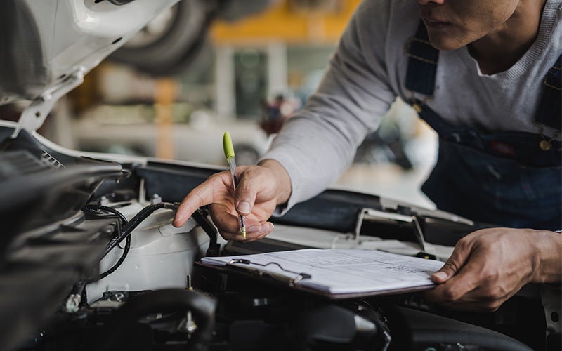 Technician reviewing an inspection checklist under the hood of a used vehicle